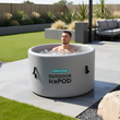 Load image into Gallery viewer, Person in an inflatable ice bath pod labeled &#39;Outdoor IcePod&#39; in a garden setting.

