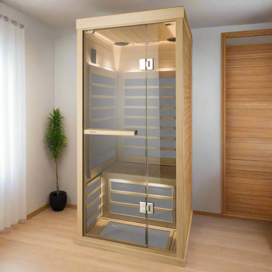 A one-person infrared sauna made of clear Hemlock wood, featuring glass walls and blue infrared panels on the floor and walls.