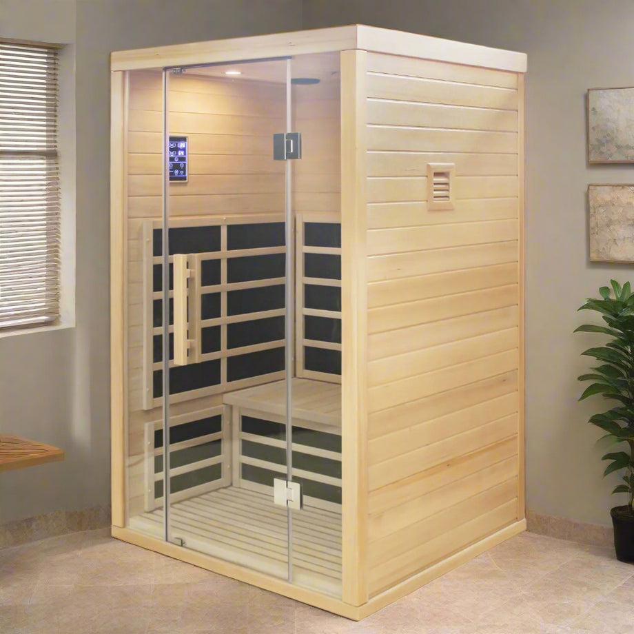 A two-person indoor infrared sauna made of light-colored wood, featuring clear glass doors and windows, with infrared panels visible on the walls and floor.